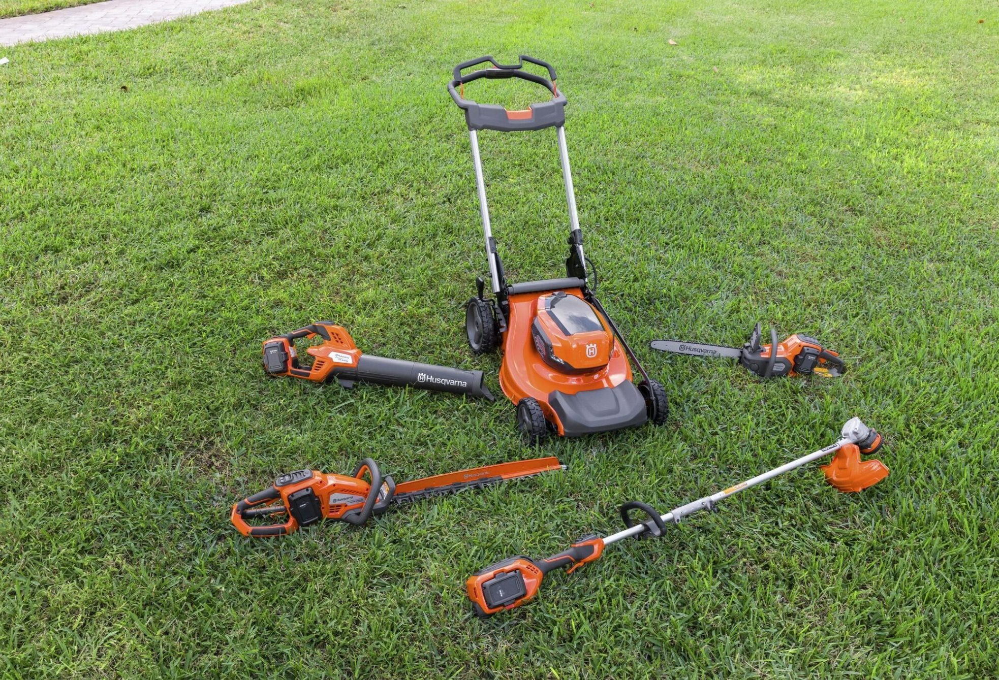 Zestaw narzędzi akumulatorowych Husqvarna na trawie - kosiarka, pilarki i podkaszarki